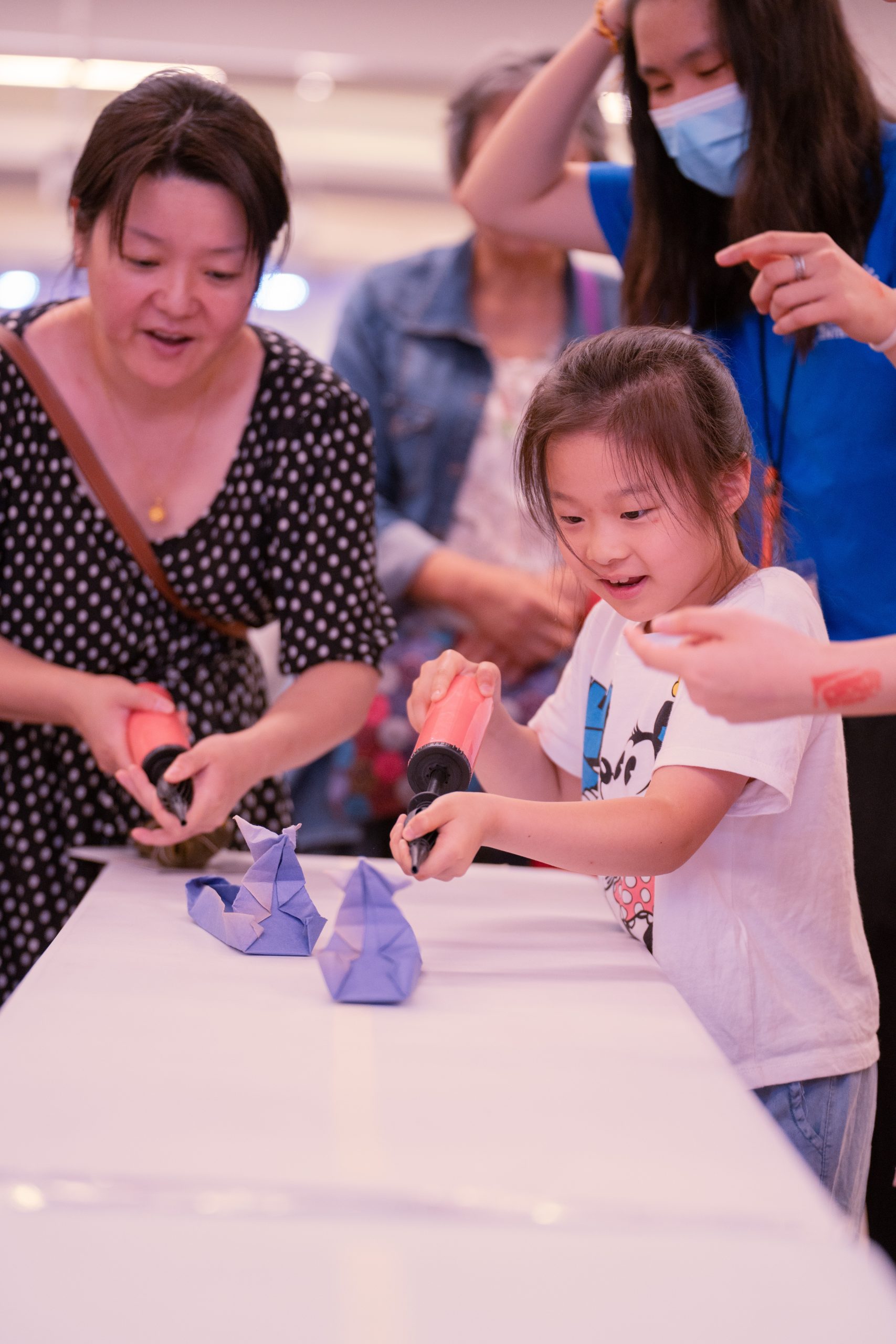 Mother and daughter trying to race two purple paper dragon boats down the table with balloon pumps (the daughter is winning)